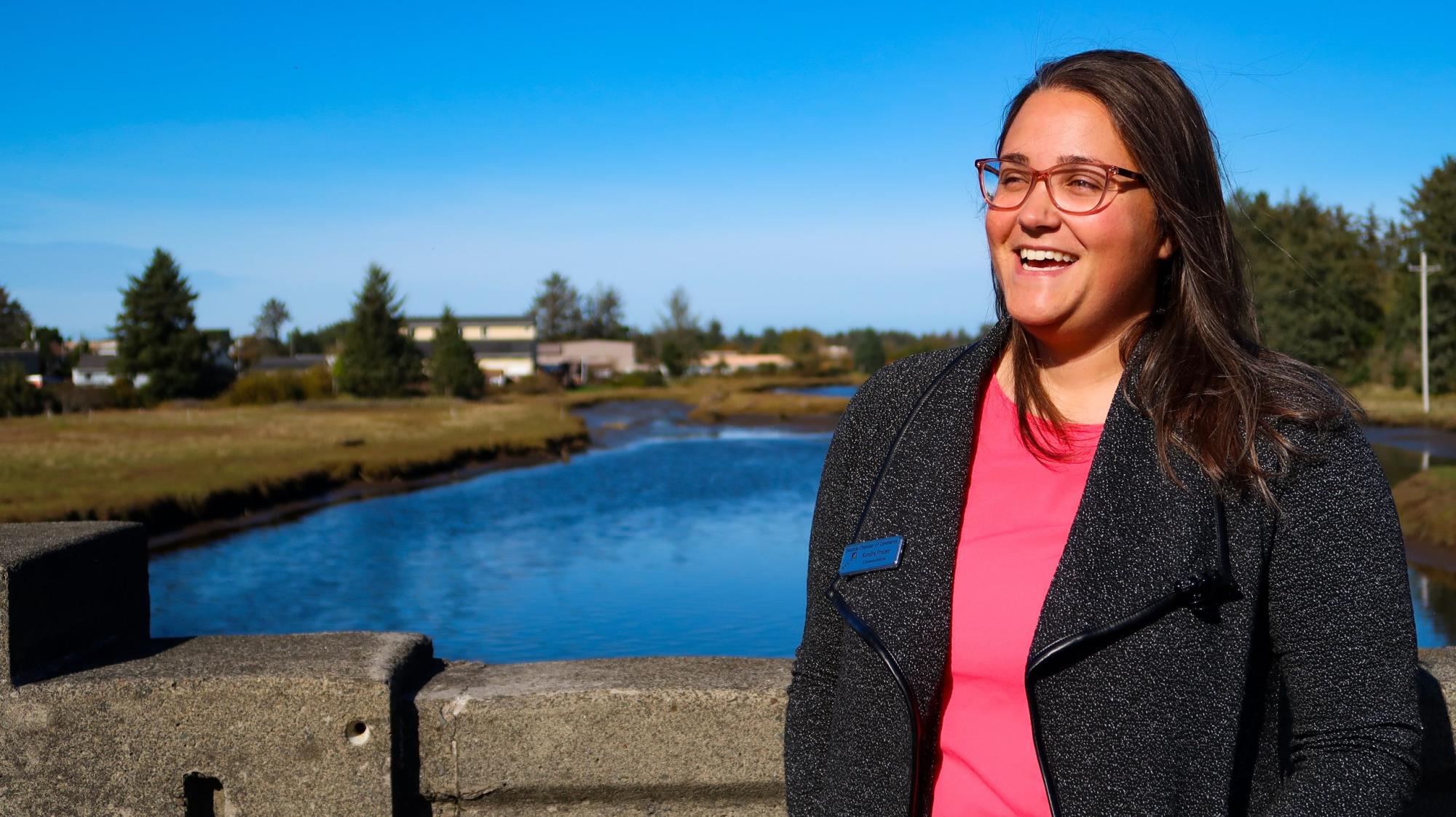 Young woman in professional outfit smiling in front of body of water