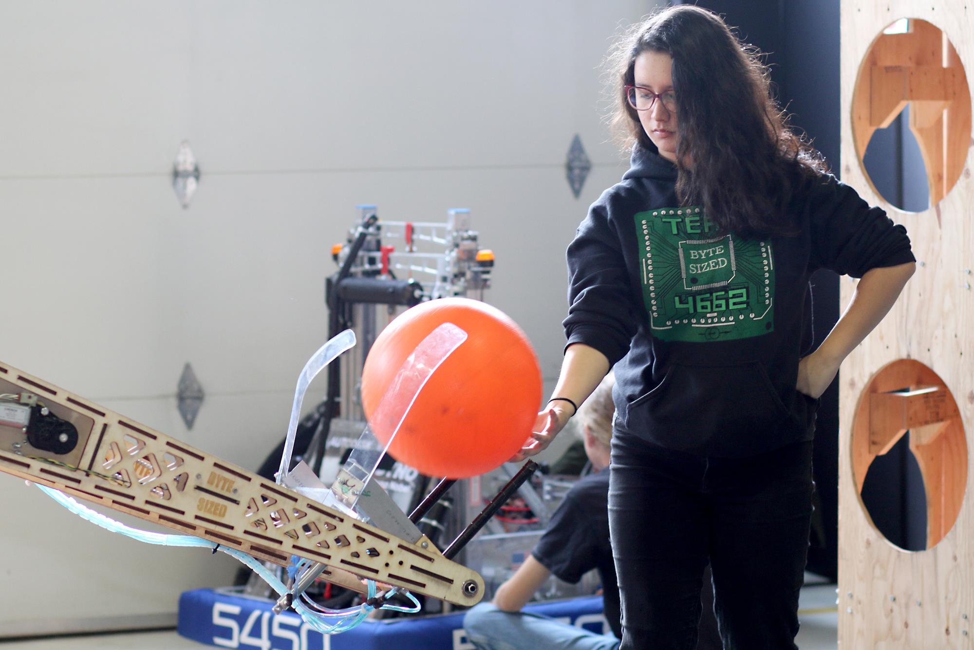 Young woman with robotics club machine with ball to use with machine