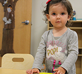 young preschool-aged girl stands behind a table