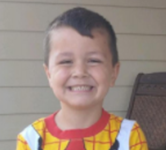 preschool student smiling at the camera with a house behind him