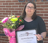 Lee Ann Banning holds a bouquet of flowers and a certificate in front of a brick building