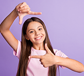 young girl with a pink shirt and a purple background with her hands making a photo around her face