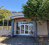 the outside of the clatsop service center has a tree, a glass door and the building is tan