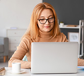 woman sitting in front of laptop at a table taking notes