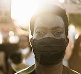 black man standing in front of a crowd wearing a black mask