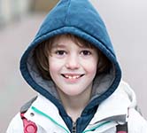 young boy stands outside with backpack