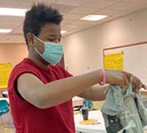 high school student in a red shirt stands inside classroom and folds a t-shirt