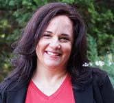 ana lia oliva stands outside in front of trees in a red shirt and black blazer