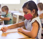 elementary students holds a pen and works on assignment at her desk