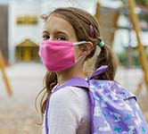 student wearing a pink mask and a purple backpack heads to school