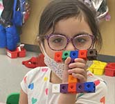 preschool-age child holds up a block in the shape of a letter i