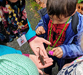 a teacher holds a newt in her palms while preschoolers look on