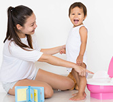 toddler stands next to a small pink and white potty with a woman nearby