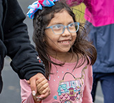 student in a pink sweatshirt and blue glasses smiles as she participates in a race