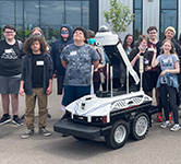 high school students stand outside next to a large white robot