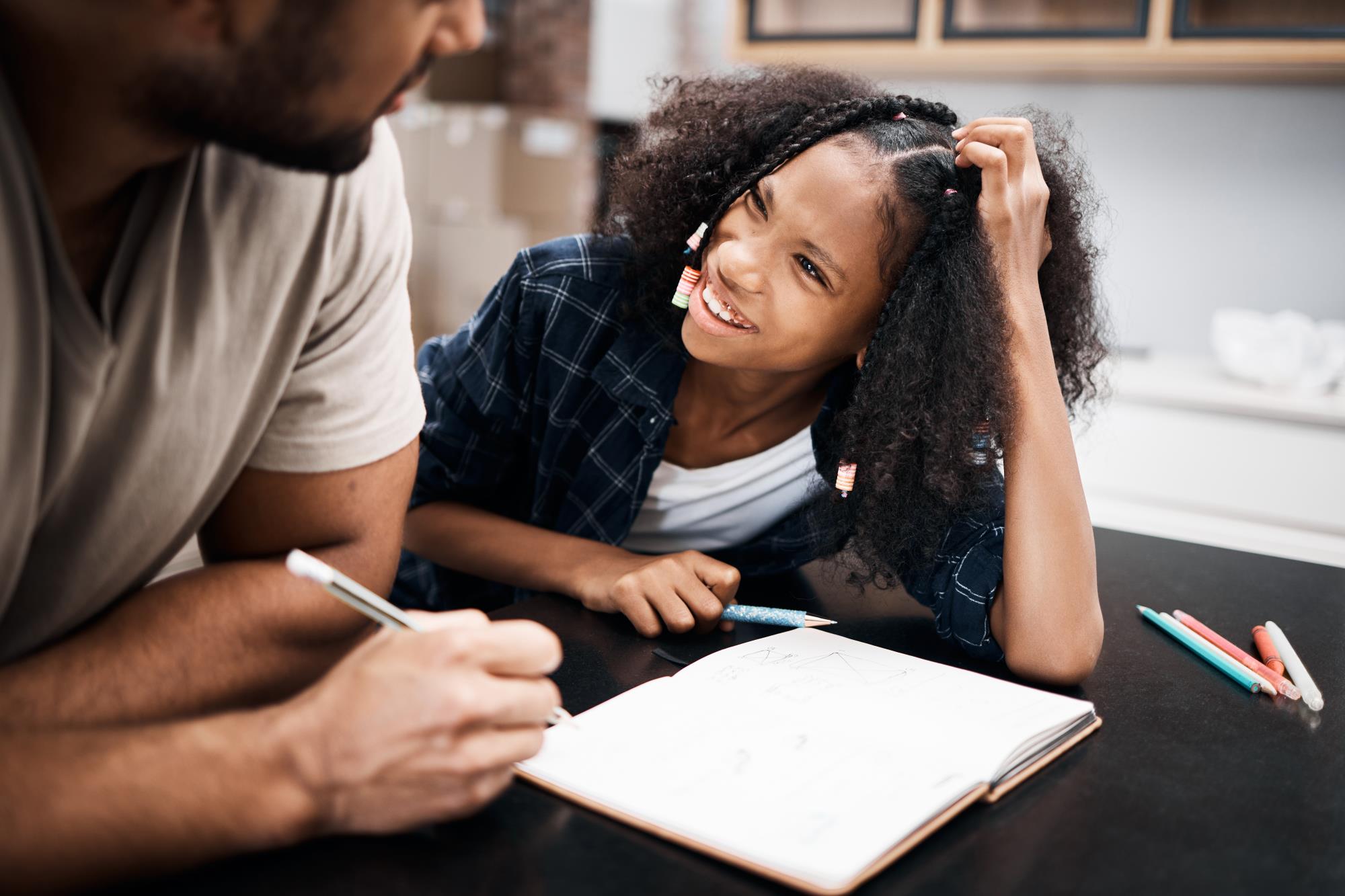 A teenage girl works on homework and looks up at her dad