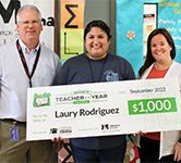 laury rodriguez stands with two educators and an enormous check for $1000