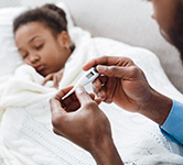 dad holds a thermometer while a child sleeps in the background