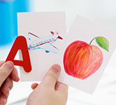 a child holds a red a with an illustration of an airplane and an apple