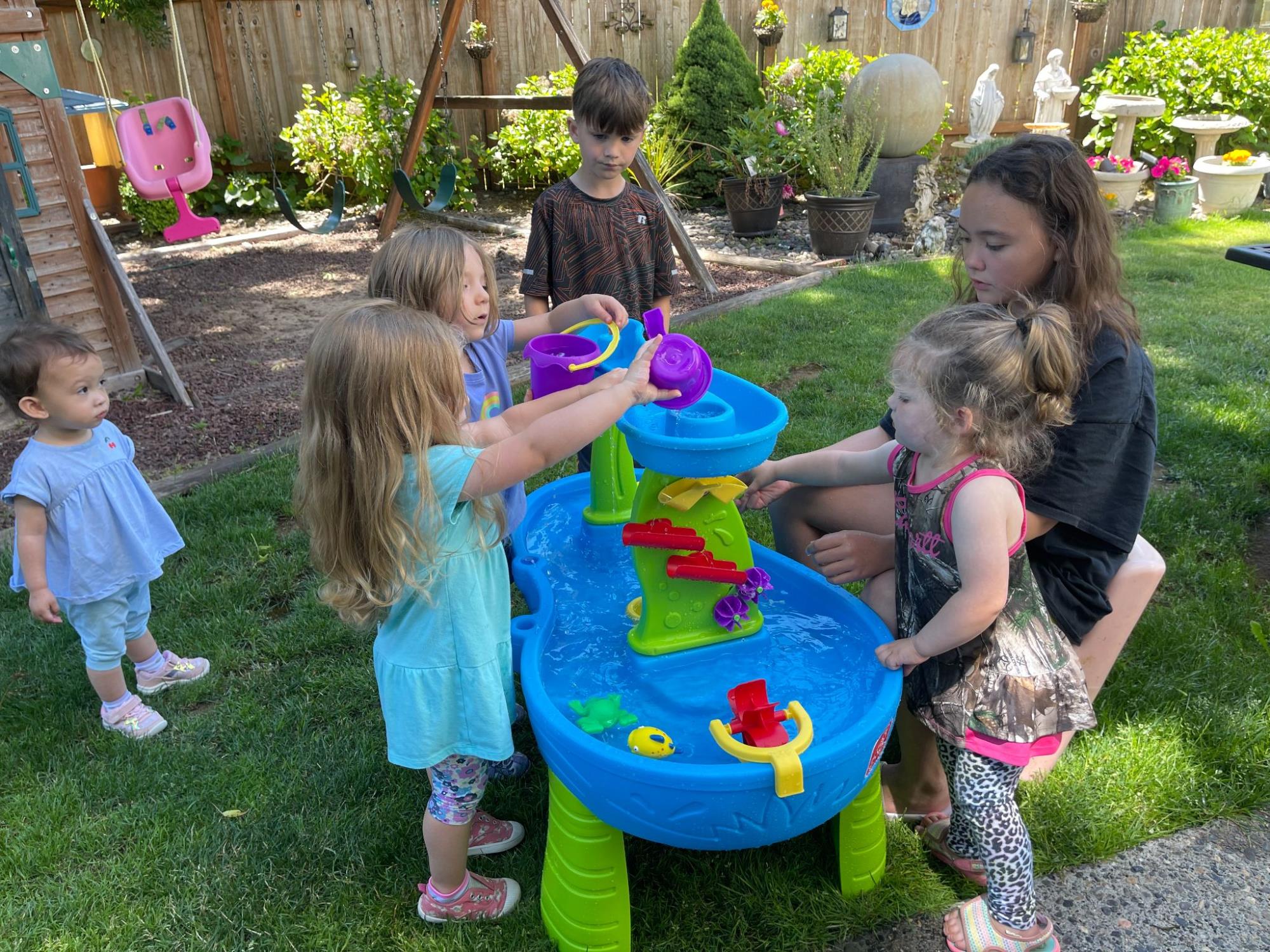 Young children play outside in the grass with a water table