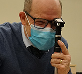 john lowery wears a mask and conducts an eye assessment