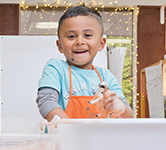 a preschooler wears an apron and plays with a bucket of water