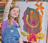 a preschooler holds her hand up in the air after she finishes painting