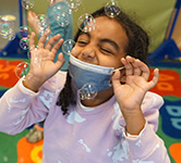 a preschooler closes her eyes as bubbles float around her