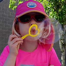 a young girl in a pink shirt blows a bubble