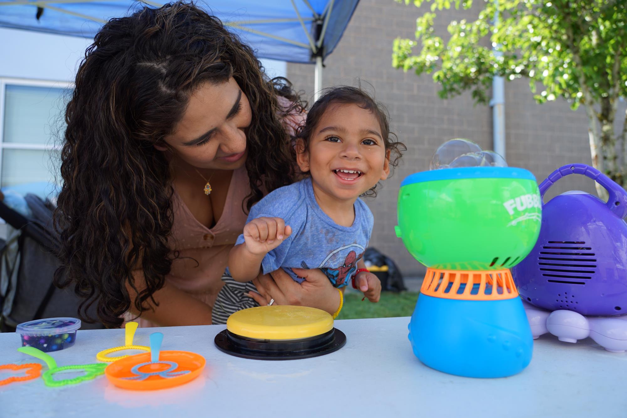 a one-year-old plays with an adaptive bubble machine as his mom holds him