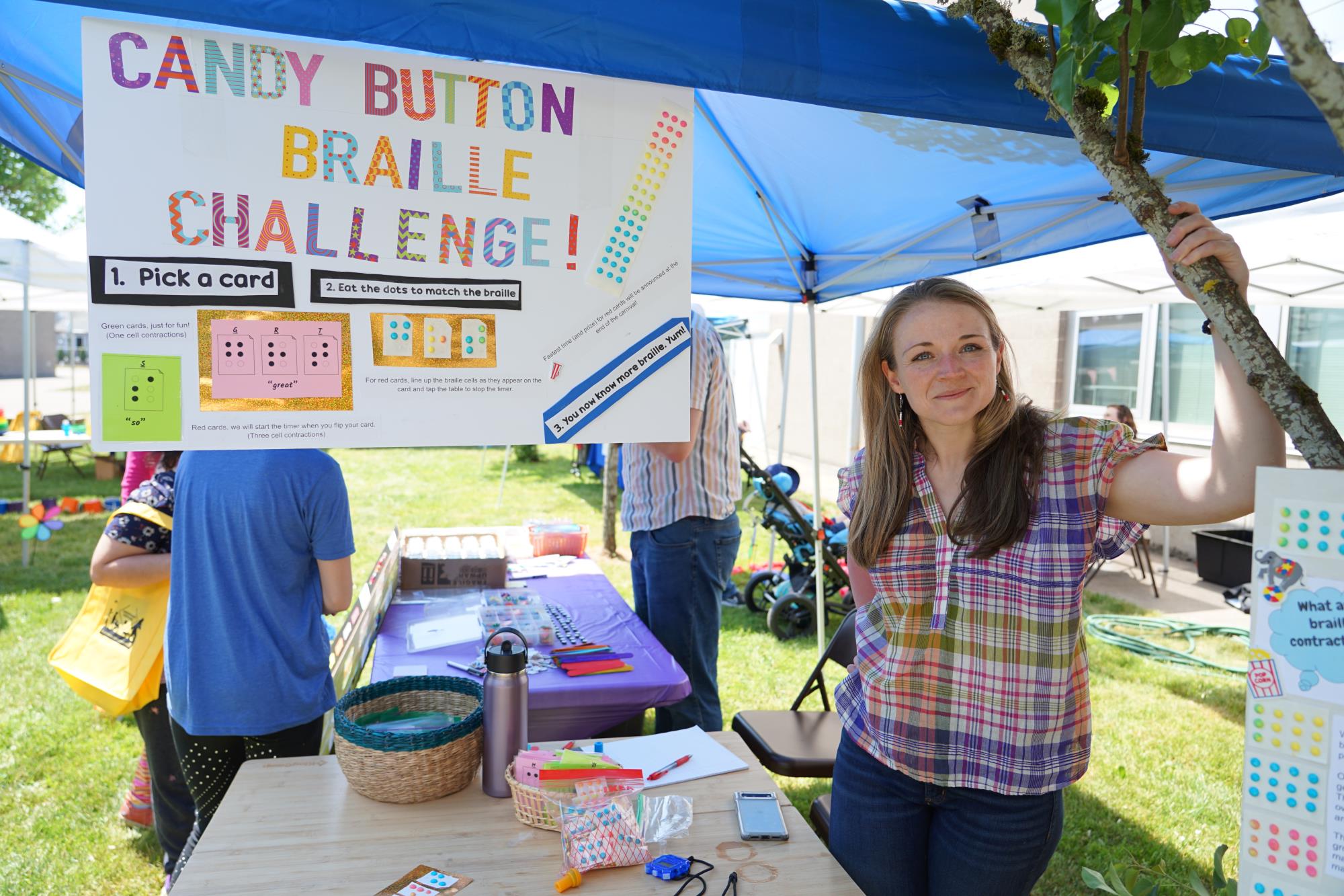 Emily Recchia stands under a blue outdoor tent at the candy button braille challenge station