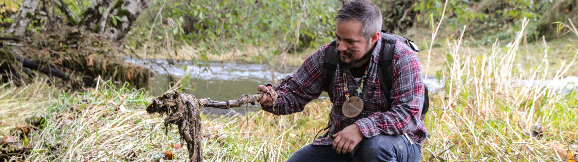 Person crouching holding a stick with wet grass on the end