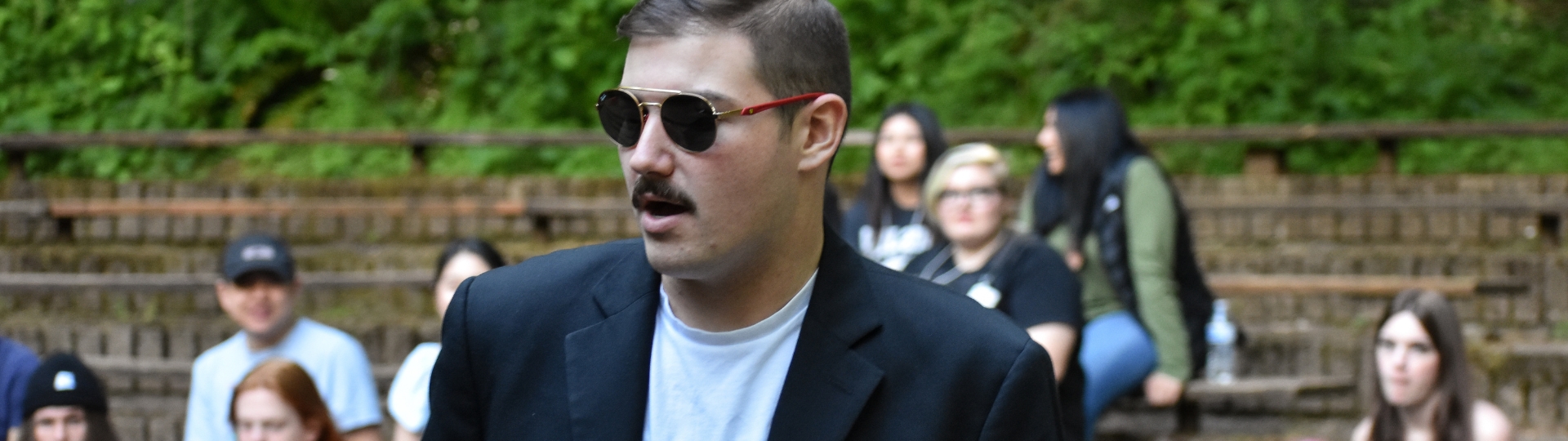 Person posing with aviator sunglasses with students blurred in background