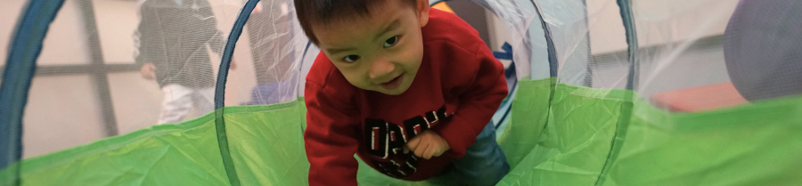 Young child crawling through a green and blue mesh play tunnel on hands and knees