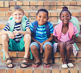 three students sit on stairs with backpacks on their backs