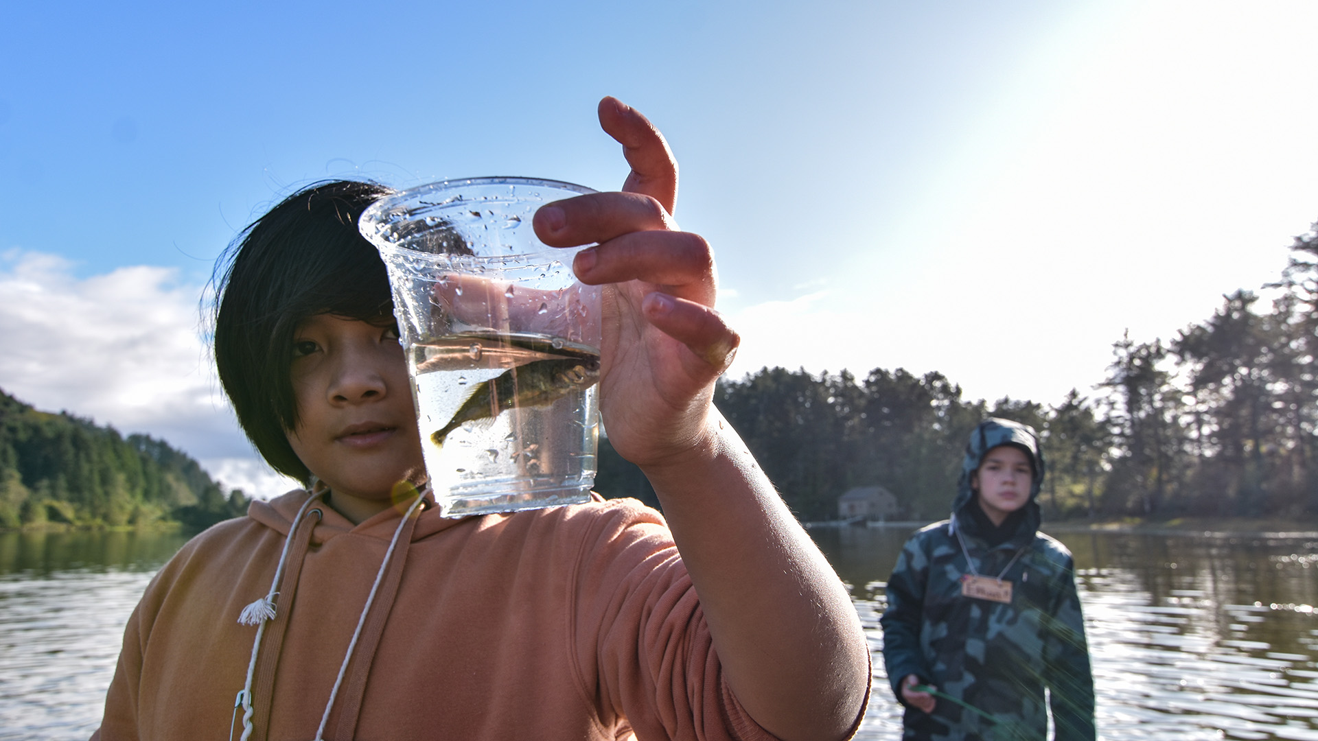 student holds up a small fish in a cup