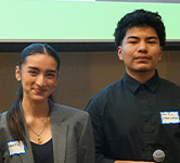 two high school students pose for a photo in a conference room