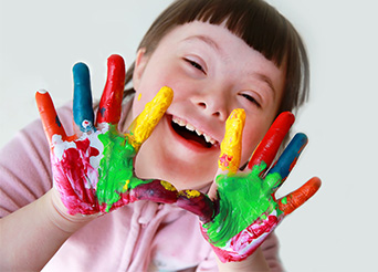 a young girl holds up her hands that are covered in paint