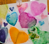 Multicolored watercolor hearts on a piece of paper sitting on a table