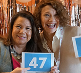 two board members pose for a photo next to rose gold balloons