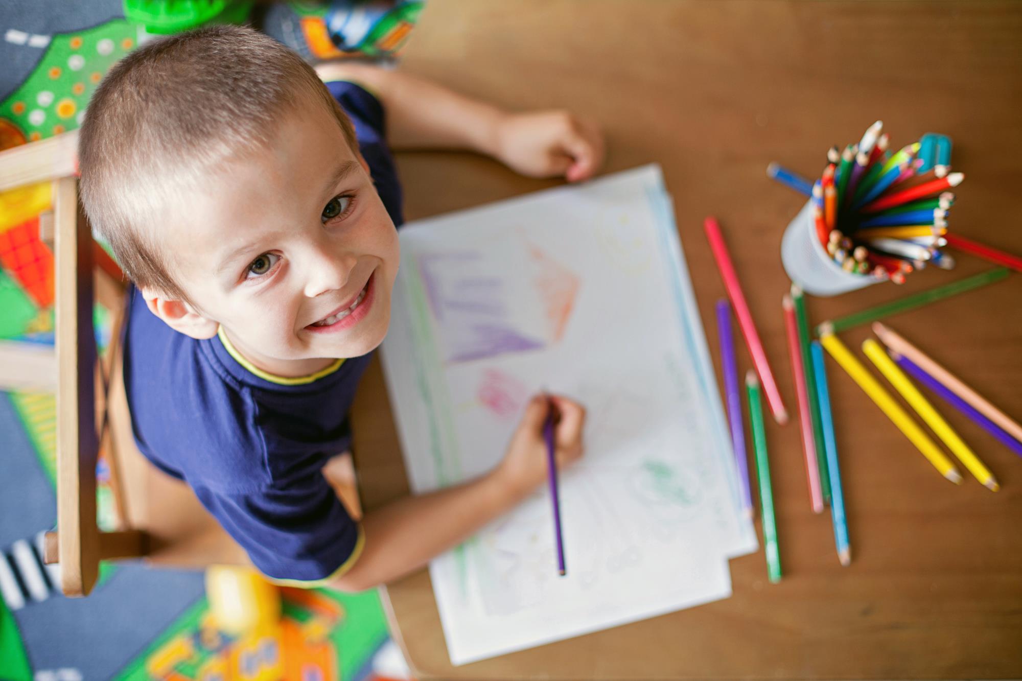 a preschooler draws with colored pencils and looks up at the camera