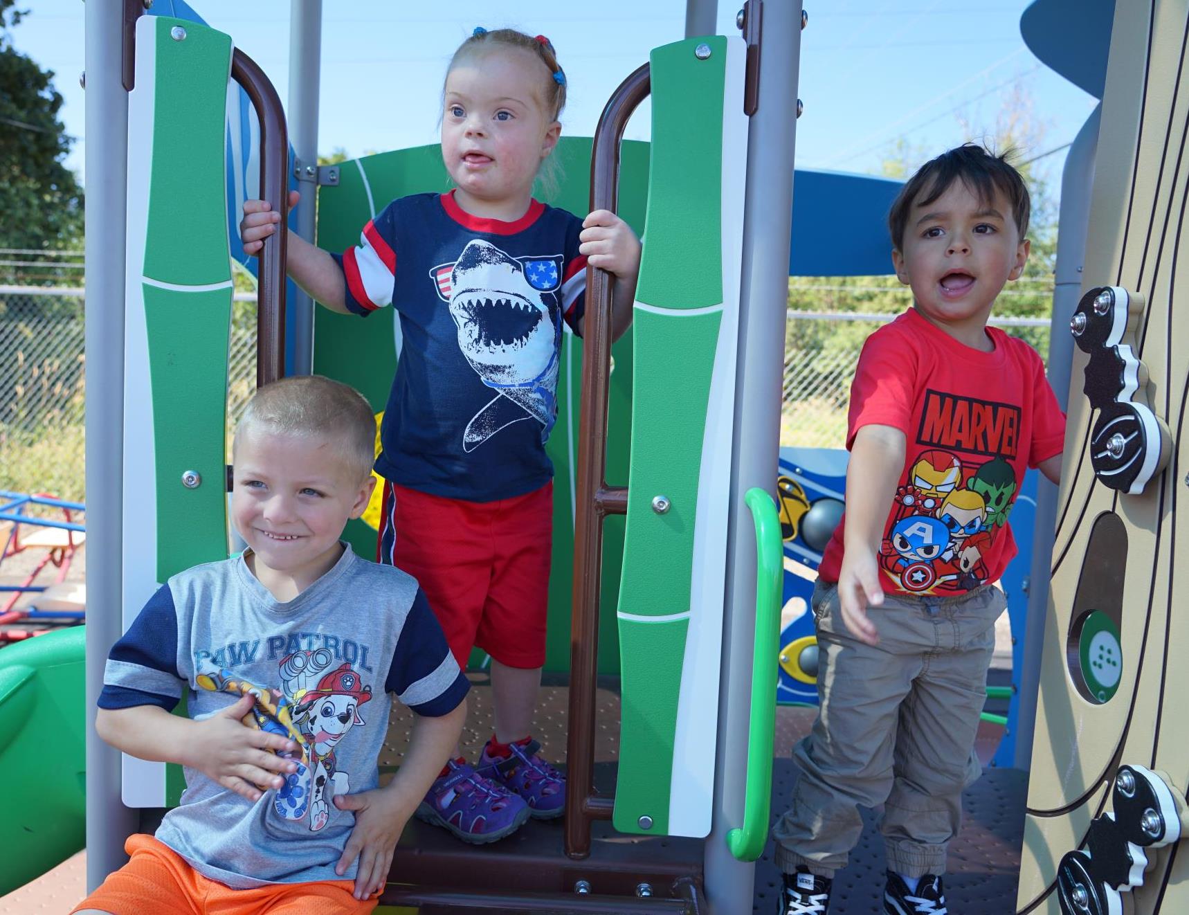 three preschoolers play on play equipment