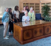 Governor Tina Kotek sits at a desk and holds up the signed attendance awareness month proclamation while education representatives stand behind her