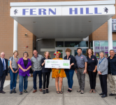 Group poses in front of Fern Hill elementary with Kayla Davidson holding a giant Oregon lottery check