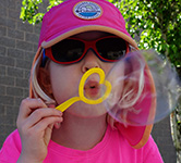 a child in a pink hat, t-shirt and sunglasses blows a bubble