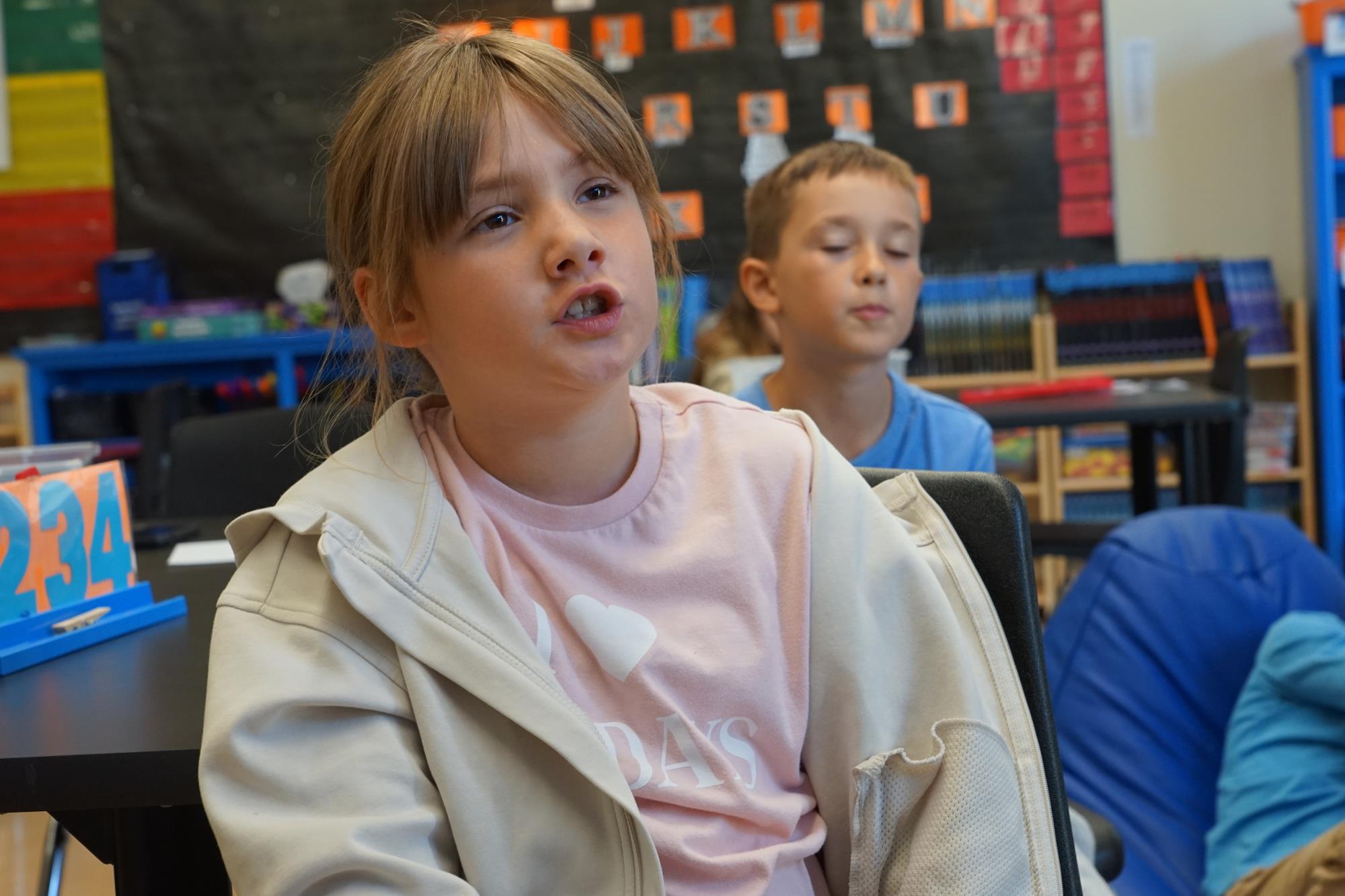 A third grade student in a pink shirt and light brain hair says the word stretch