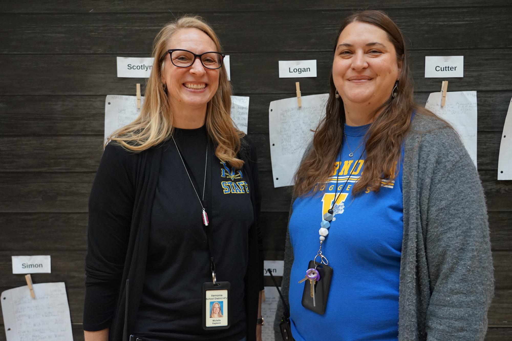 Michelle Eagleson and Kendra Schlegel pose for a photo in front of stories written by students