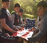 homepage photo of outdoor school students folding flag